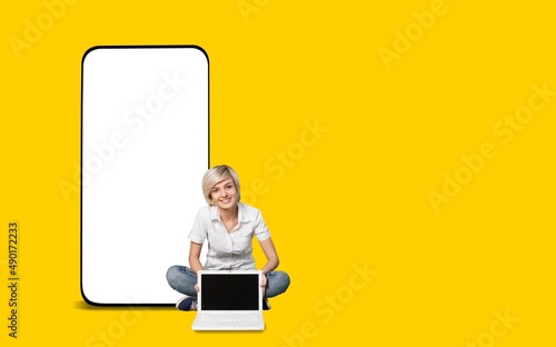 Big phone behind woman. Girl is sitting with laptop. Big blank screen smartphone.