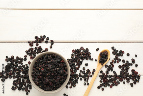 Dried black currants, bowl and spoon on white wooden table, flat lay. Space for text