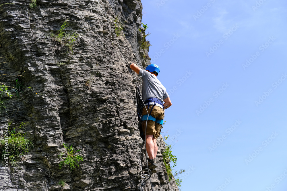 man in body harnesses feature life-safety, attaches hooks to iron brackets, climbs rock, active lifestyle of people, mountaineering, via ferrata in mountains of alps, life insurance in extreme sports