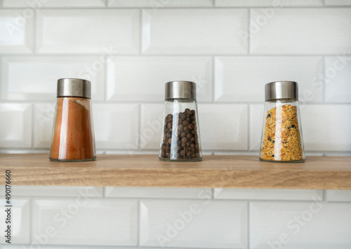 kitchen seasonings and spices in small glass jars on a kitchen countertop with a brick white wall