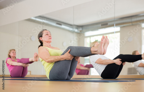 Three European mature women are doing boat pose in a fitness room