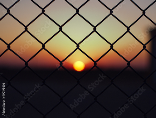 Fototapeta Closeup of chain-link fences in a field with the sunset in the blurry background