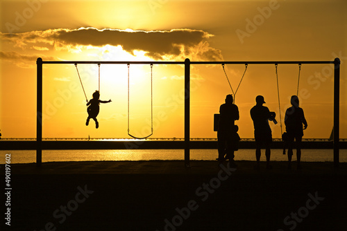 Parents and children in silhouette play on swings at sunset photo