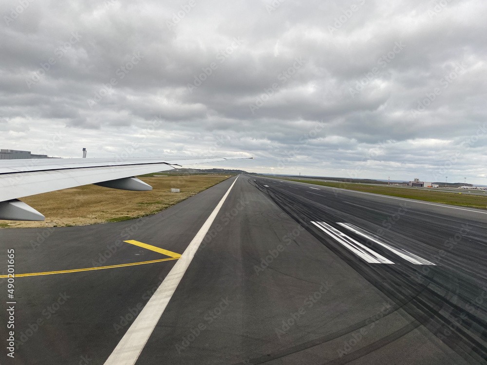 Airplane wing and airport runway with a cloudy sky in vertical Airplane wing and airport runway with a cloudy sky in vertical