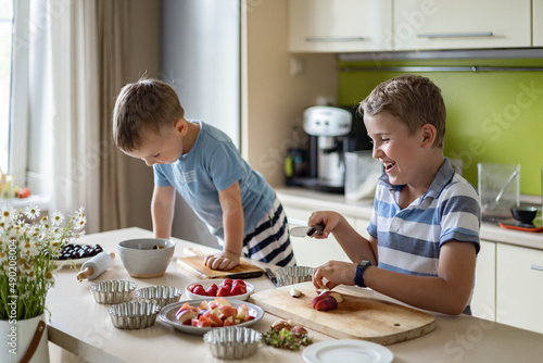 Two cute brothers cooking fresh summer dessert with fruits and berries on kitchen table