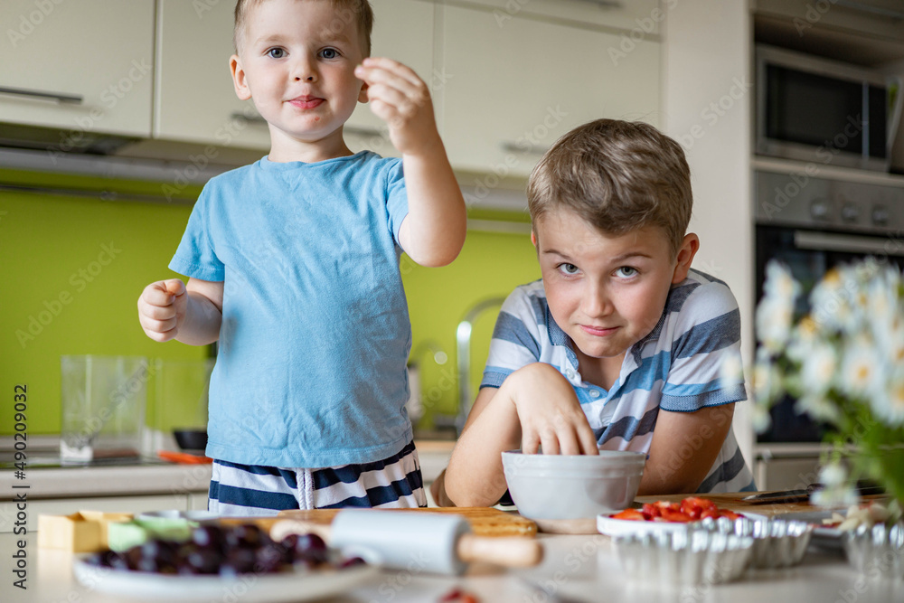 Funny brother male kids rejoicing having fun cooking summer dessert with fruits and berries