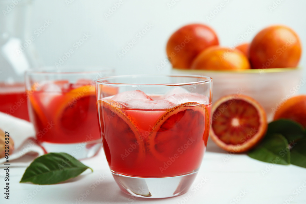 Tasty sicilian orange juice with ice cubes and fruits on white table Tasty sicilian orange juice with ice cubes and fruits on white table