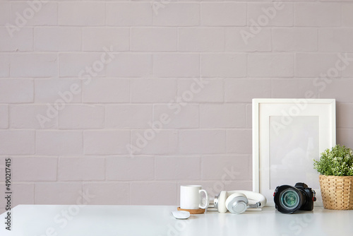 Empty picture frame, camera, coffee cup, potted plant and wireless headphone on white table.