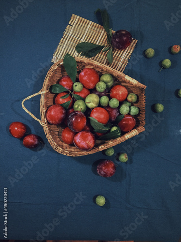 Vertical top view of colorful plums in a straw basket on a blue aesthetic background photo