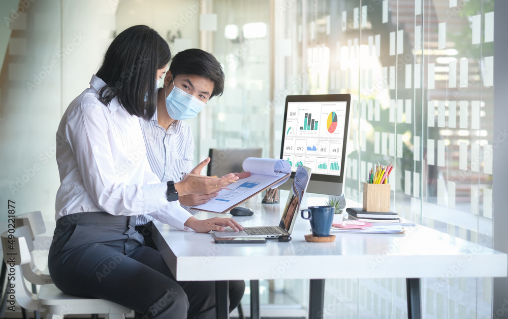 Two business people wearing protective mask working together in bright modern workplace.