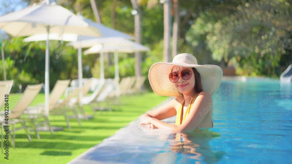 A pretty woman standing in a swimming pool wearing a huge white sun hat ...
