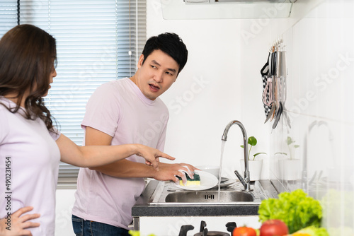 stressed couple conflict in their kitchen, angry woman pointing hand to man for washing dishes