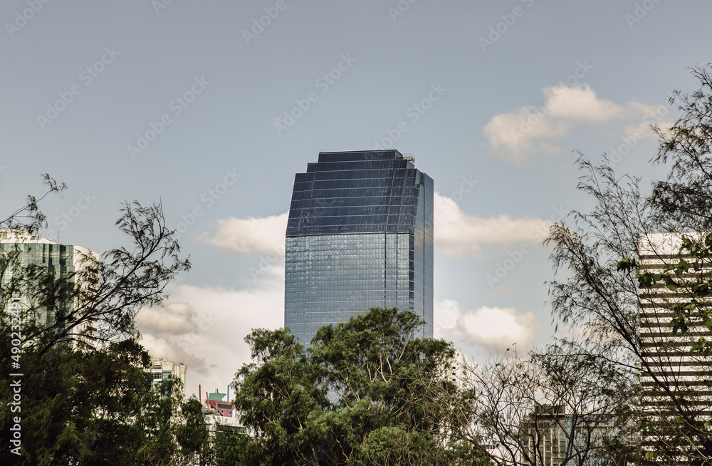 Bangkok, Thailand - Feb 19, 2022 : View of Modern high buildings among green trees space in nature against blue sky with clouds at afternoon. City growth concept, Selective focus.