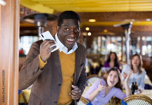 Portrait of satisfied cunning african american man stealing mobile phone of frightened upset young woman having lunch in restaurant ..