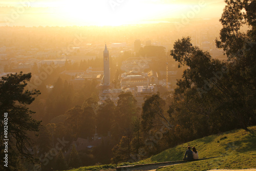 Fotografering Couple sitting on the grass near the Berkeley campanile (Sather Tower) at sunset