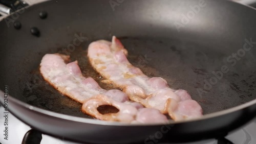 Two pieces of bacon are fried in a hot frying pan, getting ready.