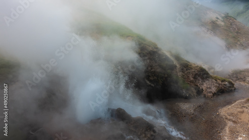 A geyser erupts on the hillside. Boiling water is visible, drops in the air. Everything is shrouded in thick steam. Poor visibility. Kamchatka. Valley of Geysers