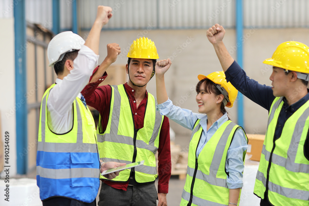 Group of technician engineer and businessman in protective uniform with hardhat standing and raising hands celebrate successful together or completed deal commitment at industry manufacturing factory Group of technician engineer and businessman in protective uniform with hardhat standing and raising hands celebrate successful together or completed deal commitment at industry manufacturing factory