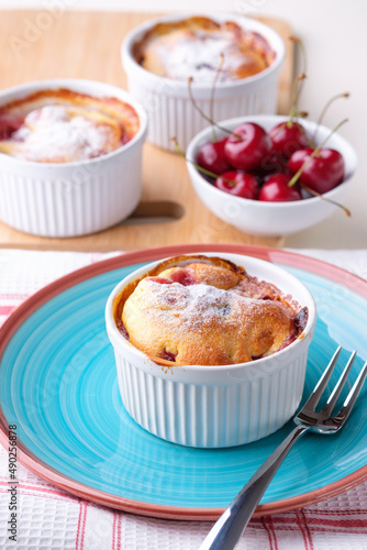Traditional french baked cherry pie clafoutis served in white ramekin and some cherry on the table. Vertical.