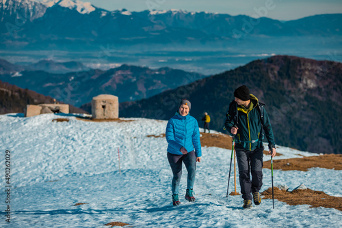 Young couple, male and female are hiking on a snow covered hill or mountain. Winter hike on Blegos, sunny hill in slovenian alps.