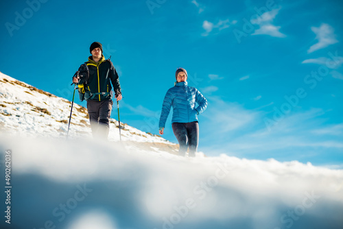 Young couple, male and female are hiking on a snow covered hill or mountain. Winter hike on Blegos, sunny hill in slovenian alps. photo