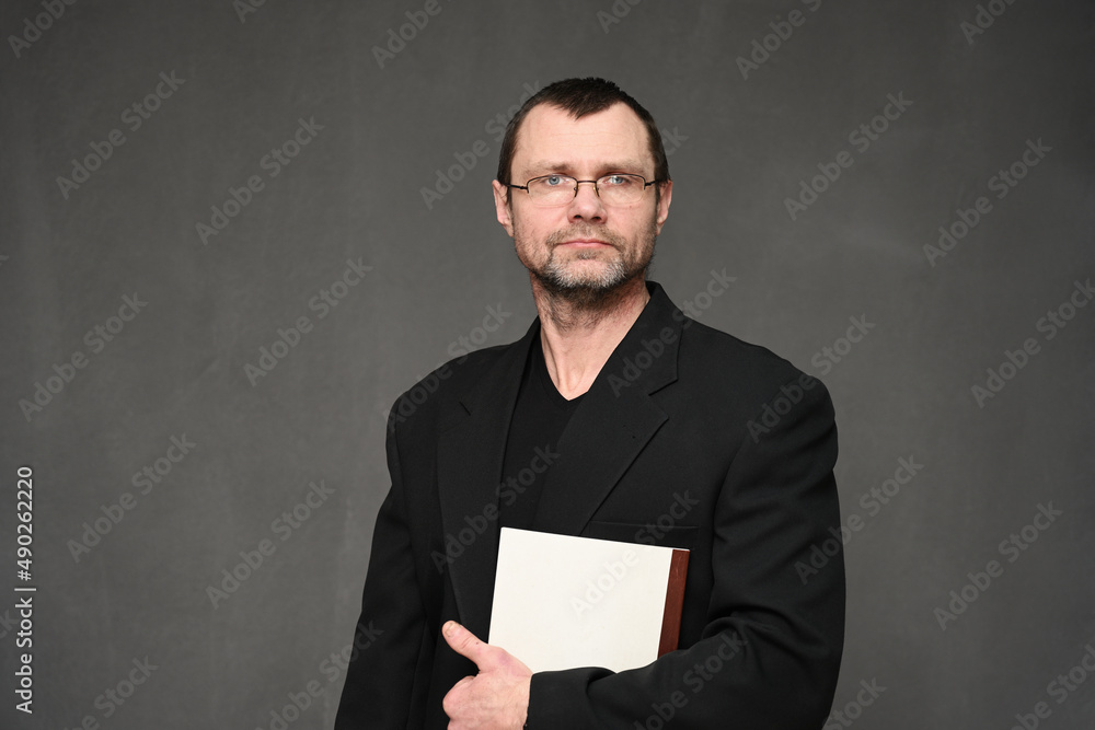 A businessman in a jacket looks at the camera with a folder in his hands. Portrait on a gray background in the studio A businessman in a jacket looks at the camera with a folder in his hands. Portrait on a gray background in the studio