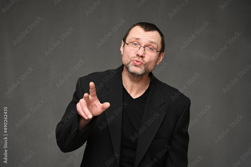 Businessman in a jacket and glasses with emotions talking to the camera. Portrait of an adult man on a gray background in the studio
