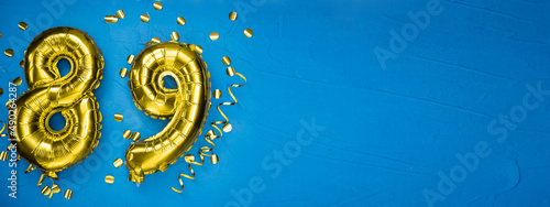golden yellow foil balloon on blue concrete background number eighty nine. Birthday or anniversary card with 89 inscription. Anniversary celebration. photo