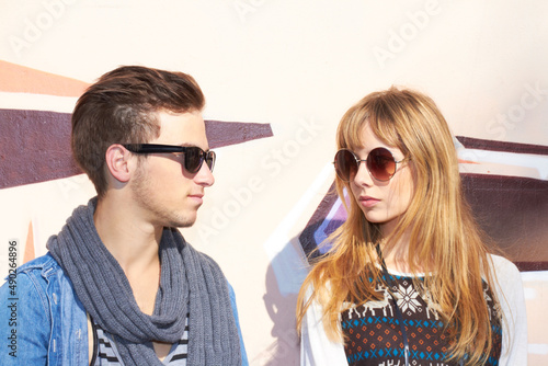 The sun shines on us 247. A young and stylish couple standing outside wearing sunglasses.