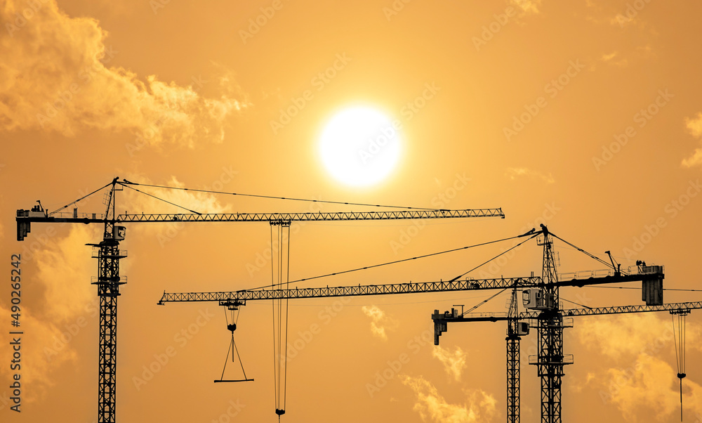 Silhouettes of tower construction cranes with yellow sky at morning time