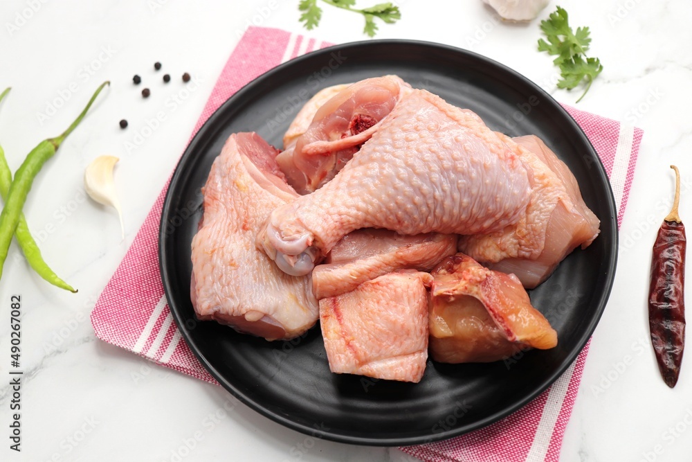 Clean and Raw Chicken on a black plate with Indian spices and cooking ingredients. Along with copy space. Chicken curry cut. Biryani cut chicken with skin on. complete animal based Protein source. Clean and Raw Chicken on a black plate with Indian spices and cooking ingredients. Along with copy space. Chicken curry cut. Biryani cut chicken with skin on. complete animal based Protein source.