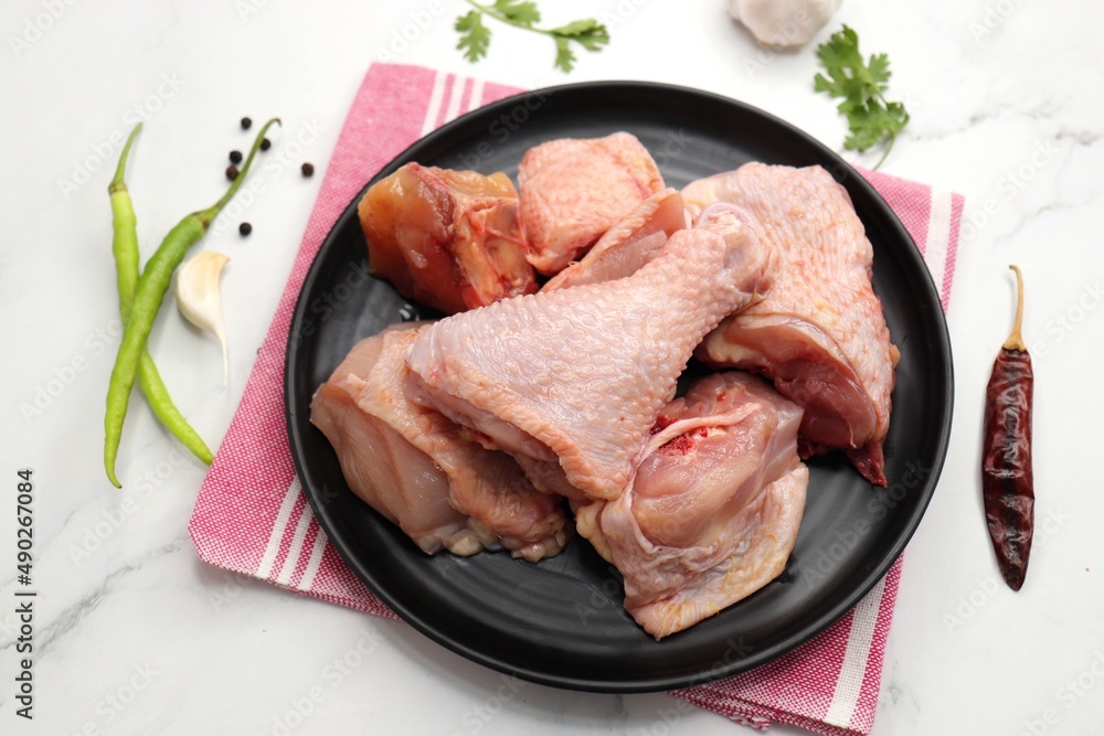 Clean and Raw Chicken on a black plate with Indian spices and cooking ingredients. Along with copy space. Chicken curry cut. Biryani cut chicken with skin on. complete animal based Protein source. Clean and Raw Chicken on a black plate with Indian spices and cooking ingredients. Along with copy space. Chicken curry cut. Biryani cut chicken with skin on. complete animal based Protein source.