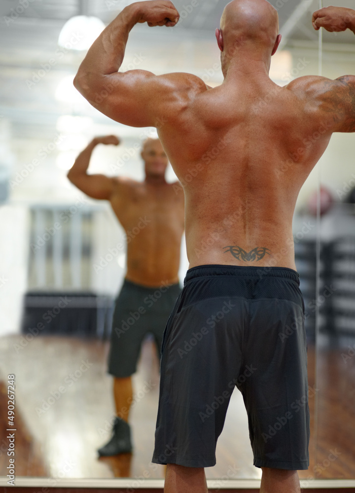 His hard work is paying off. Rearview shot of a male bodybuilder flexing his muscles at the gym in front of the mirror. His hard work is paying off. Rearview shot of a male bodybuilder flexing his muscles at the gym in front of the mirror.