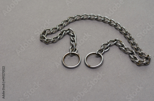 Silver metal chain with two rings on a gray background. Tugging dog leash.