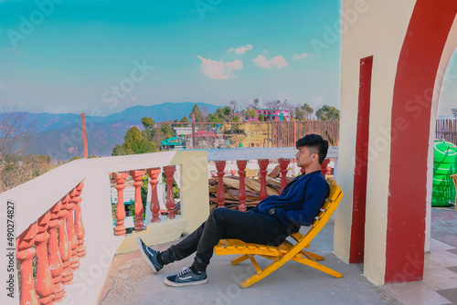 Indian boy sitting on a chair on the balcony, relaxing on a chair, enjoying the view from the terrace, mountain view from the top