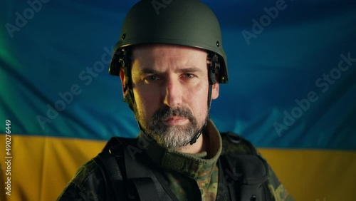 Close-up of Ukrainian soldier in military uniform and helmet looking at camera with flag at background. photo