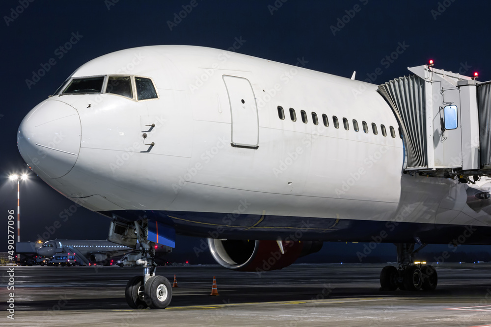 Obraz premium Close-up white wide body passenger aircraft stands at the boarding bridge on night airport apron
