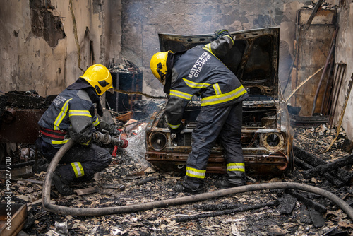 A car fire in workshop or house garage. Firefighters extinguishing fire in car with fire hoses and water. Explosion and fire disaster. Translation : "Firefighters"