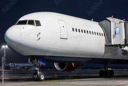 Close-up white wide body passenger aircraft stands at the boarding bridge on night airport apron