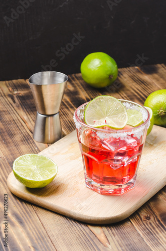 Red cocktail with lime on a wooden table.