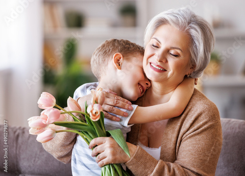 Cheerful little boy giving flowers to grandmother photo