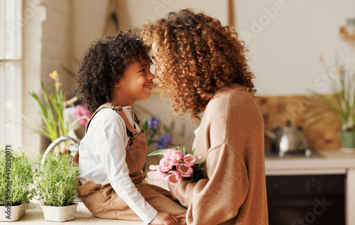 Young  ethnic woman mother with flower bouquet embracing son while getting congratulations on Mother's day
