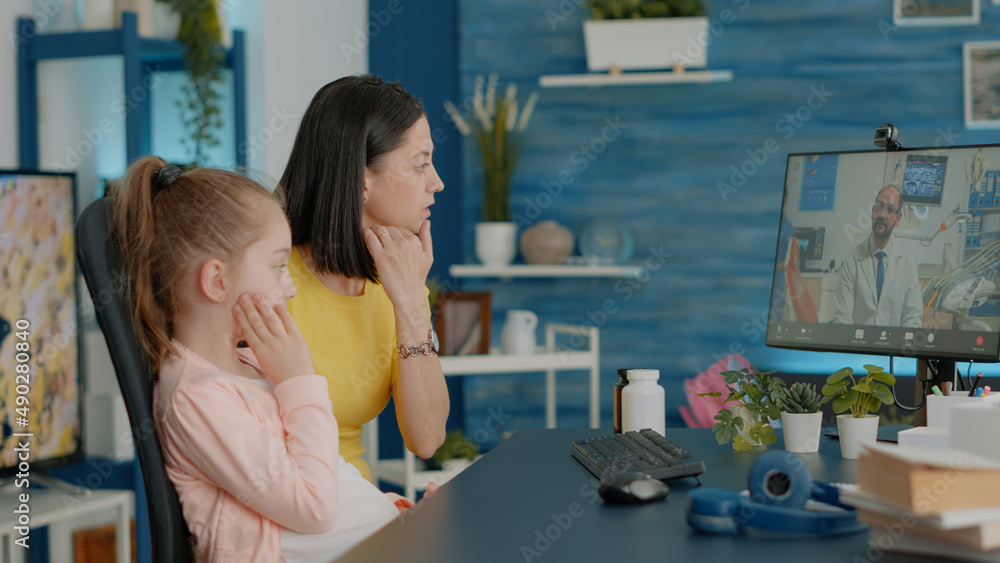 Mother of girl with toothache talking to dentist on video call for oral care advice and treatment to cure pain. Parent using online conference for remote consultation and telemedicine Mother of girl with toothache talking to dentist on video call for oral care advice and treatment to cure pain. Parent using online conference for remote consultation and telemedicine
