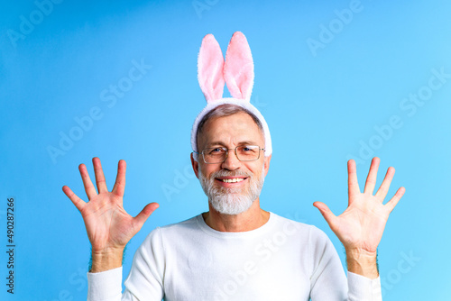 Cute mature man with bunny ears ready to Easter festivale on blue color background photo