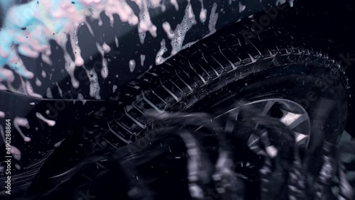 The car moving though automatic car wash machine. The brush moving to clean tires and rim. Slow motion shot
