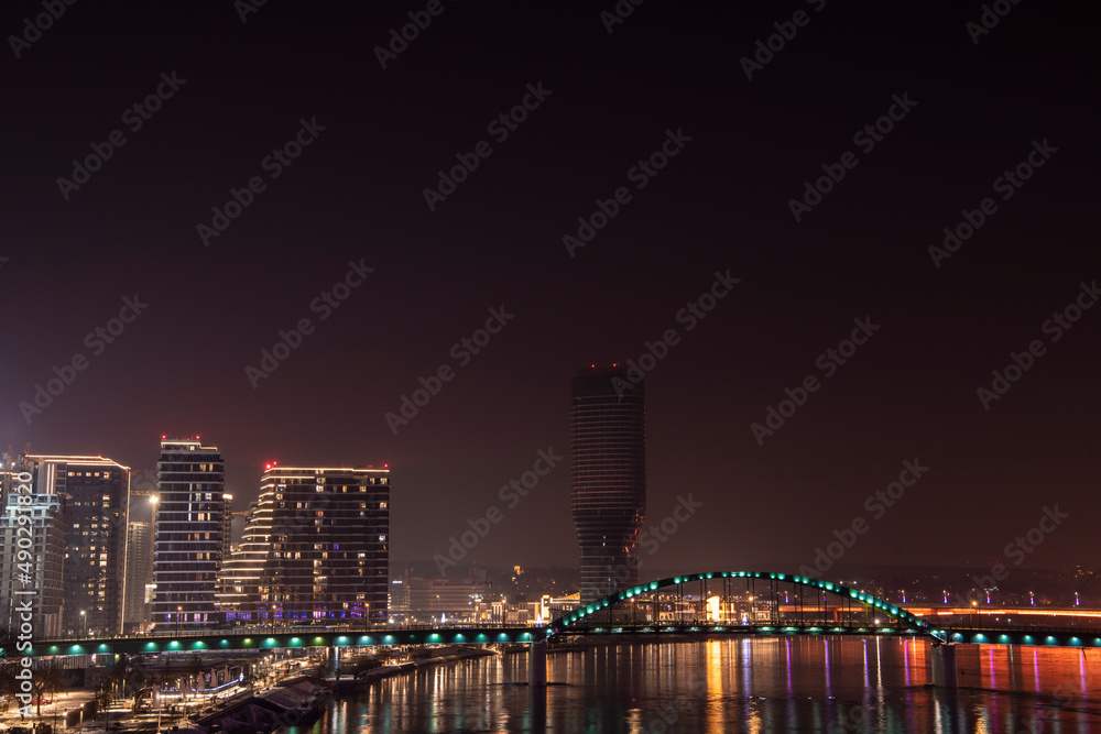 Obraz premium Beautiful scenic view over city center and business district at night with reflection in water at river Sava in Belgrade Waterfront. Belgrade, Serbia