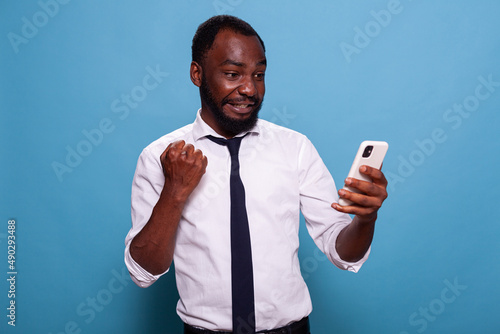 Man in white shirt holding smartphone winning online mobile game looking tensed at screen. Gamer testing mobile app on smart phone for the first time feeling enthusiastic. © DC Studio