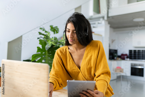 Photography indian woman telecommuting from home, with headphones, computer and tablet