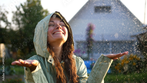 Young happy woman wearing green raincoat is feeling free and smiling under the rain. Concept of life, freedom, nature, adventure, purity.