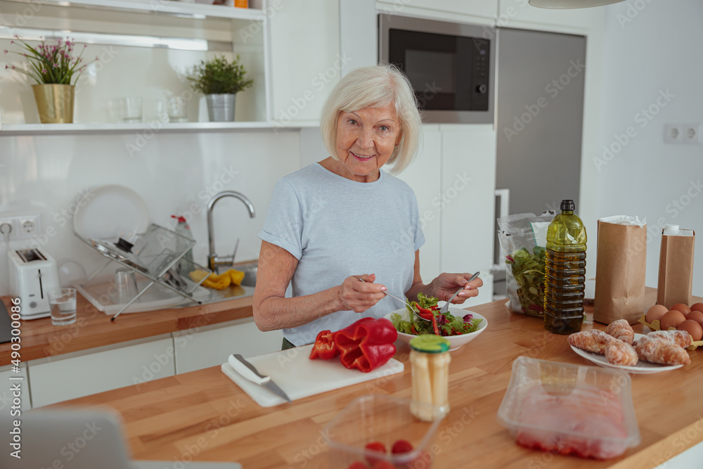 Pension age good looking woman eating green salad indoors